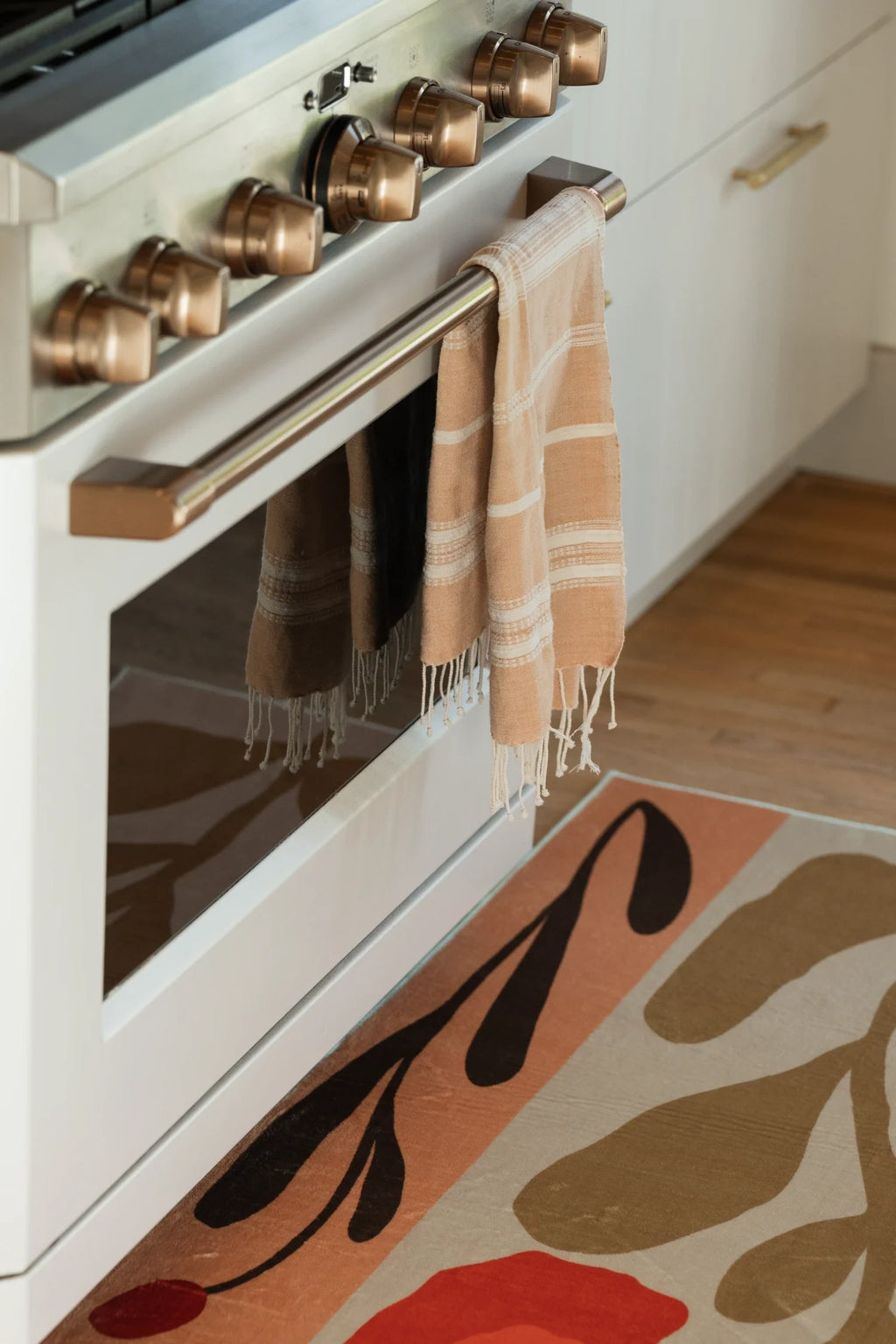 Close up of the vintage patchwork rug beside the oven door, showing beige floral silhouettes and rust red blocks