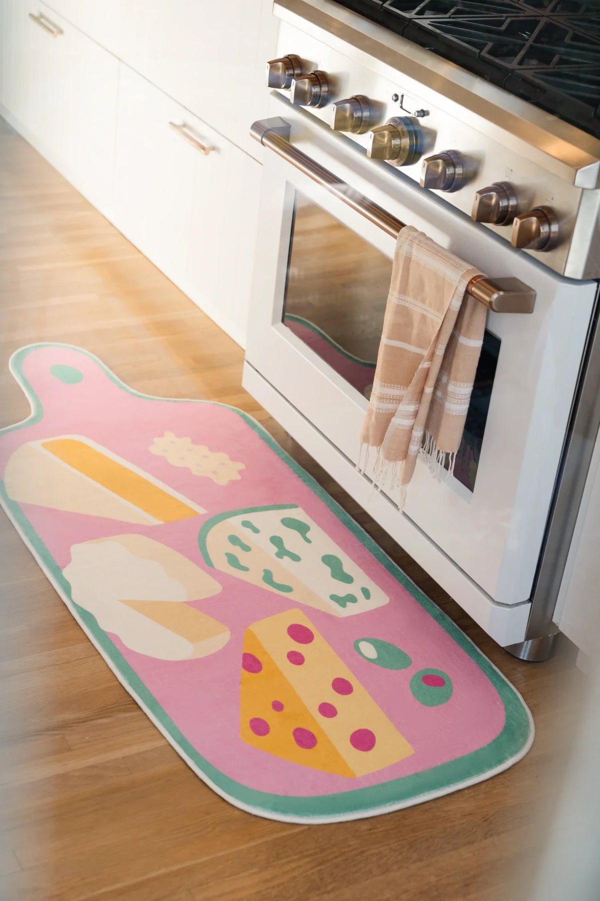 Pink cheese platter runner rug beside a white kitchen oven on a light wood floor, with playful snack motifs