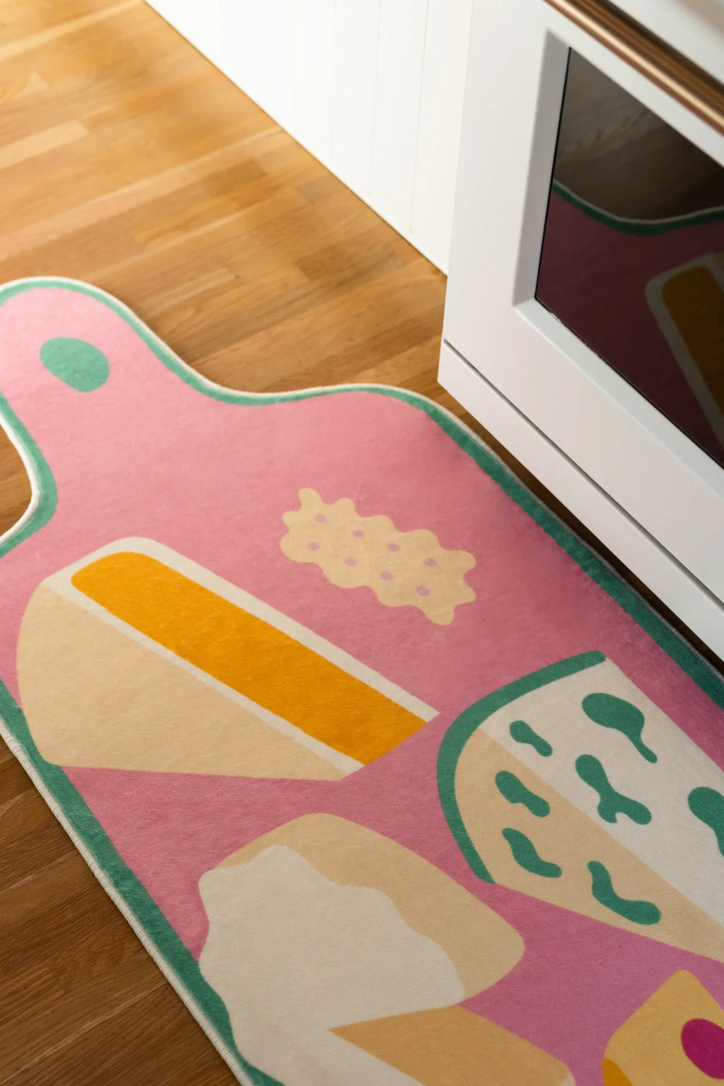 Graphic cheese platter runner in front of a white oven, with a rounded board shape and pastel food illustrations