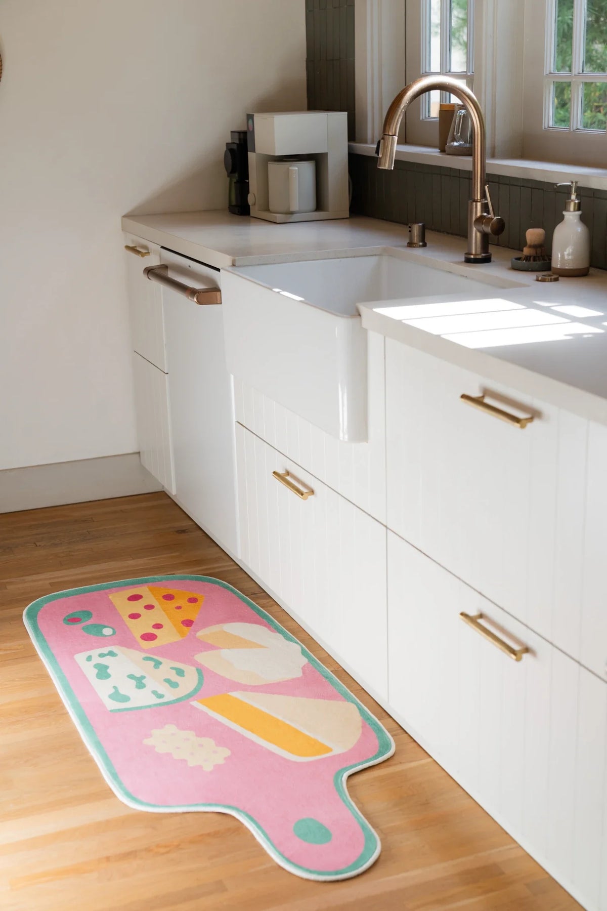 Pink kitchen runner rug beside white cabinetry and a sink area, showing a cheese board design on a light wood floor