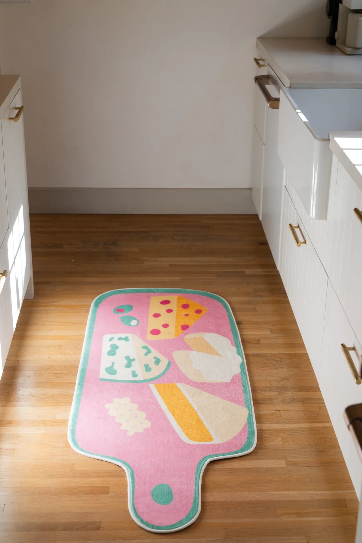 Pink irregular shaped runner rug between white lower cabinets, styled like a cheese board with colorful appetizer forms