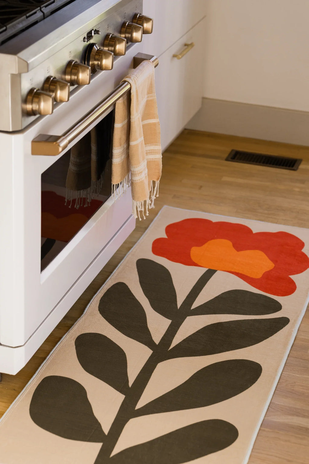 Floral runner placed in front of a white range, with rounded red petals and bold dark leaves on a cream ground