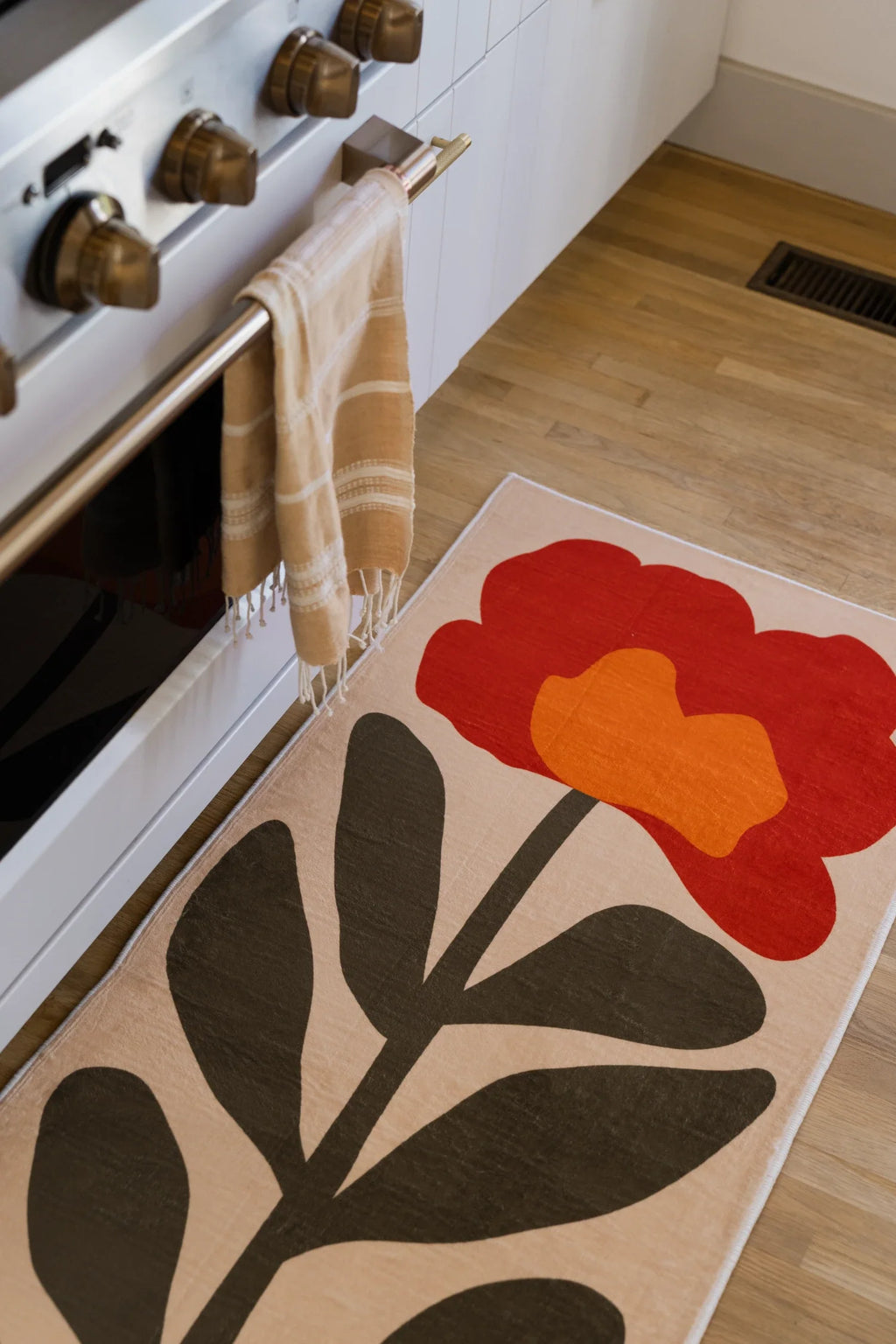 Close view of the flower runner next to the oven, showing a red bloom, orange center, and dark leaf stem