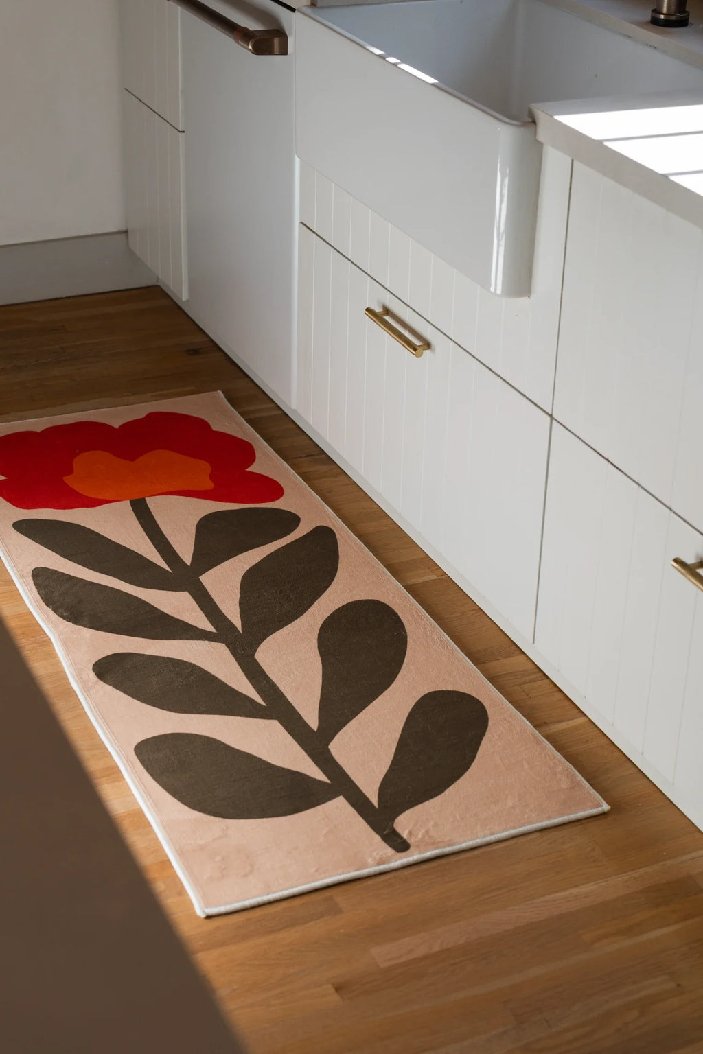 Flower runner rug in a bathroom vanity area with white cabinets, light wood flooring, and a bold botanical motif