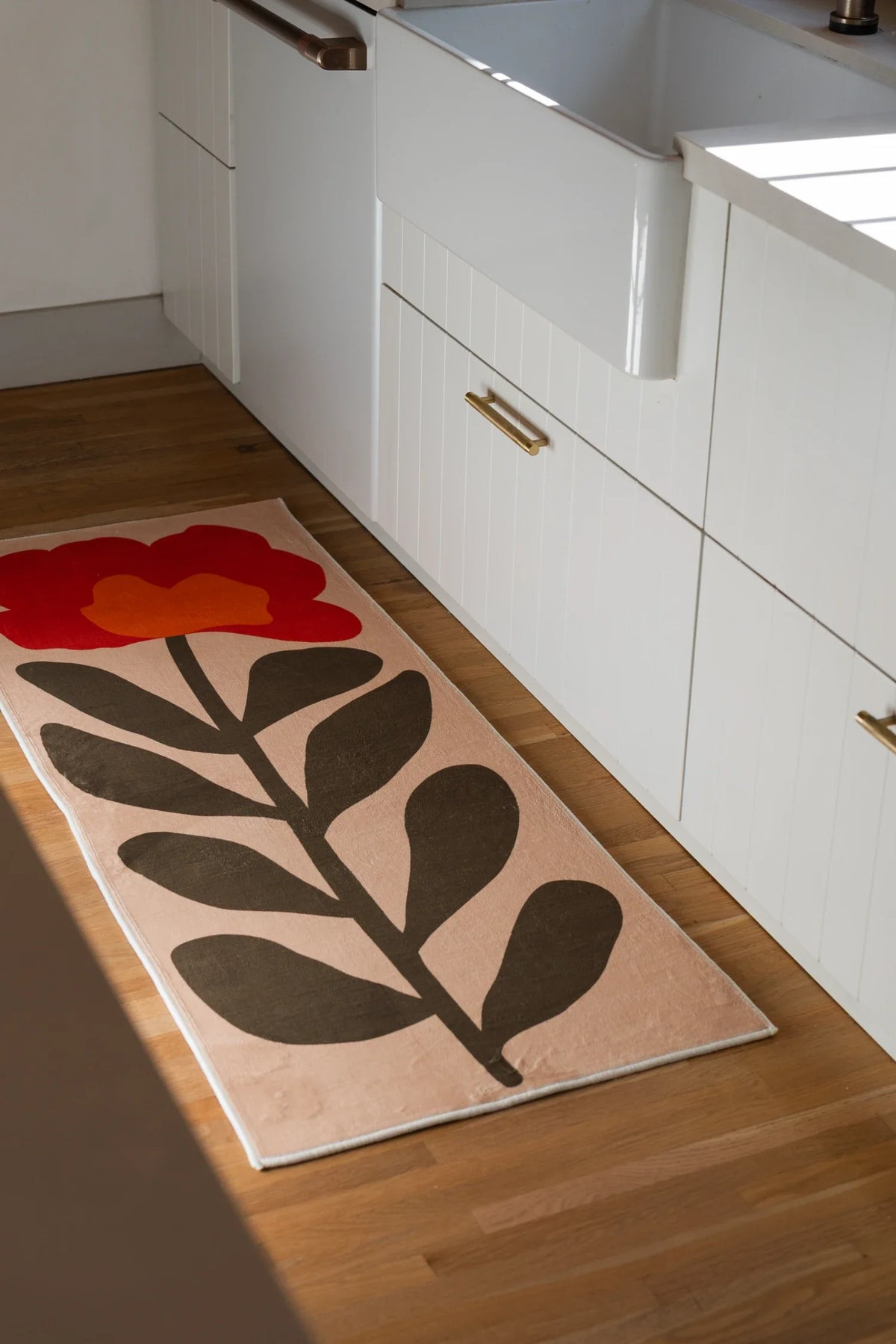 Flower runner rug in a bathroom vanity area with white cabinets, light wood flooring, and a bold botanical motif