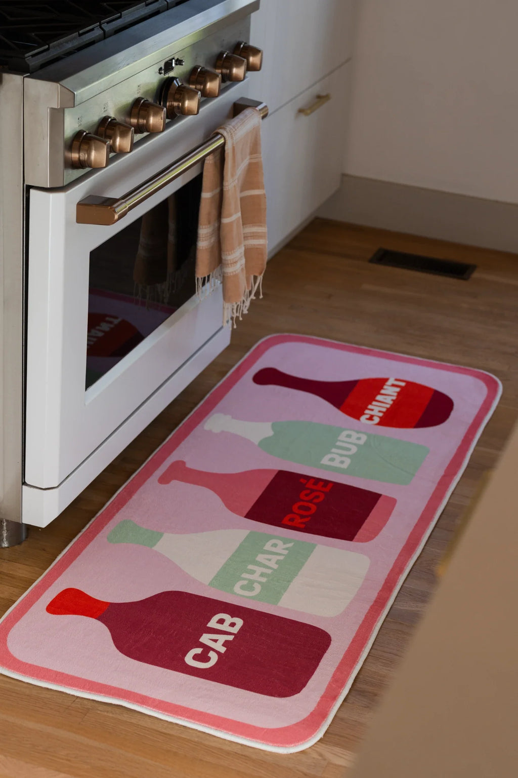 Pink graphic wine bottle runner rug beside a white kitchen oven on a light wood floor