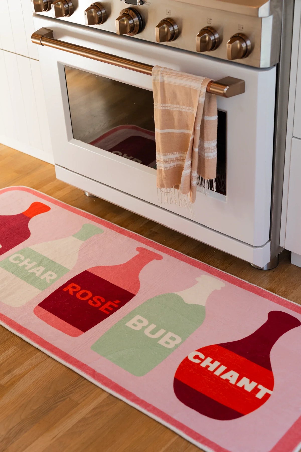 Graphic bottle runner rug in front of a white oven, with pink, red, and sage bottle motifs on a soft pink ground