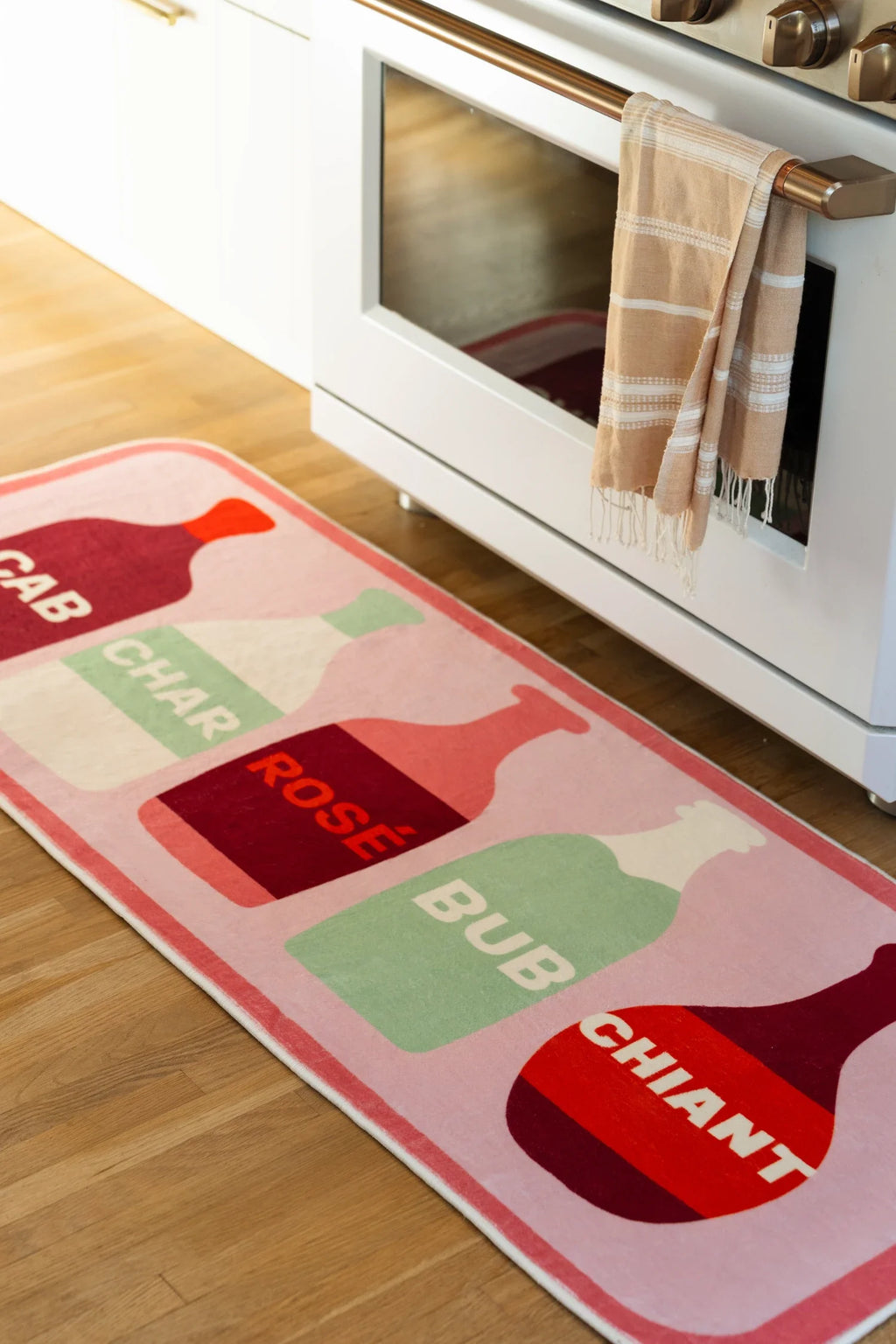 Pink kitchen runner rug with wine bottle graphics beside white cabinetry and a light wood floor