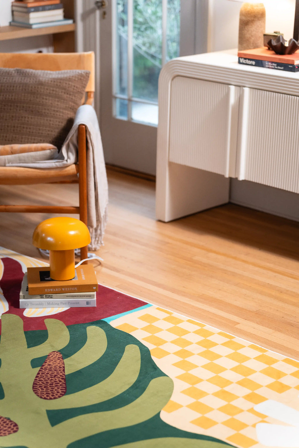 Yellow checkerboard blocks, green leaves, and brown seed pods beside a white cabinet, stacked books, and yellow lamp.