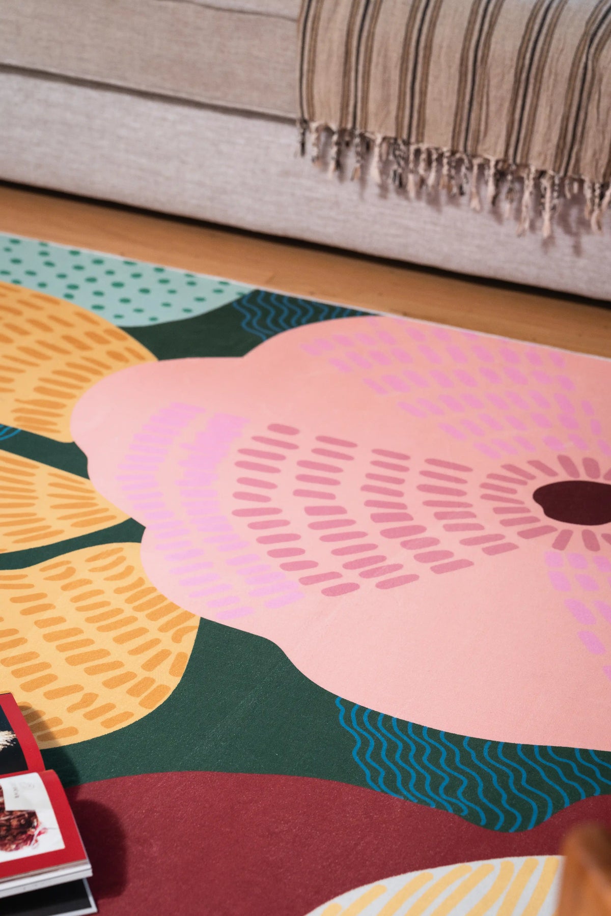 Large pink flower and layered green, mustard, and teal leaves beneath a gray sofa with a striped throw.