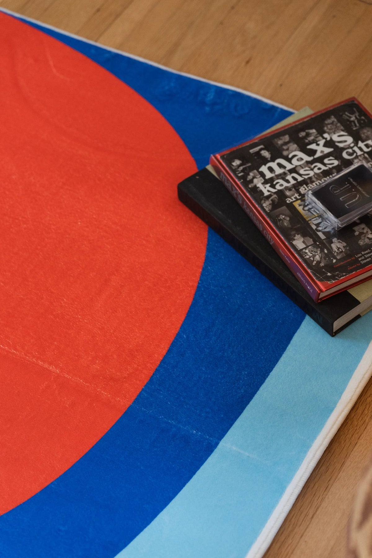 Rug corner close up with a black book on the blue and red Tomato Twist rug, showing red and blue curved bands