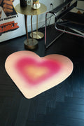 Heart-shaped pink rug on a dark wooden floor with a poster and small table in the background.