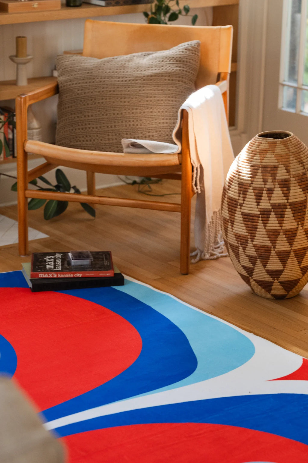 Blue and red rug near a wood chair and woven basket, showing curved red and blue bands on a wood floor
