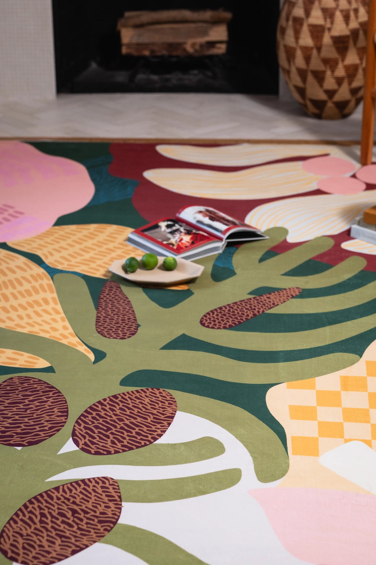 Cream petals, green leaves, brown pods, and yellow checks beside a fireplace and carved wooden vase.