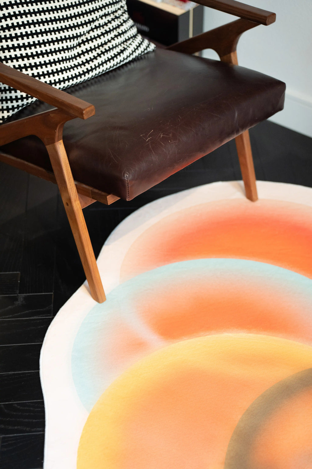 Earth Tone Abstract Circle Rug beside a brown leather chair with sunlight falling across the edge
