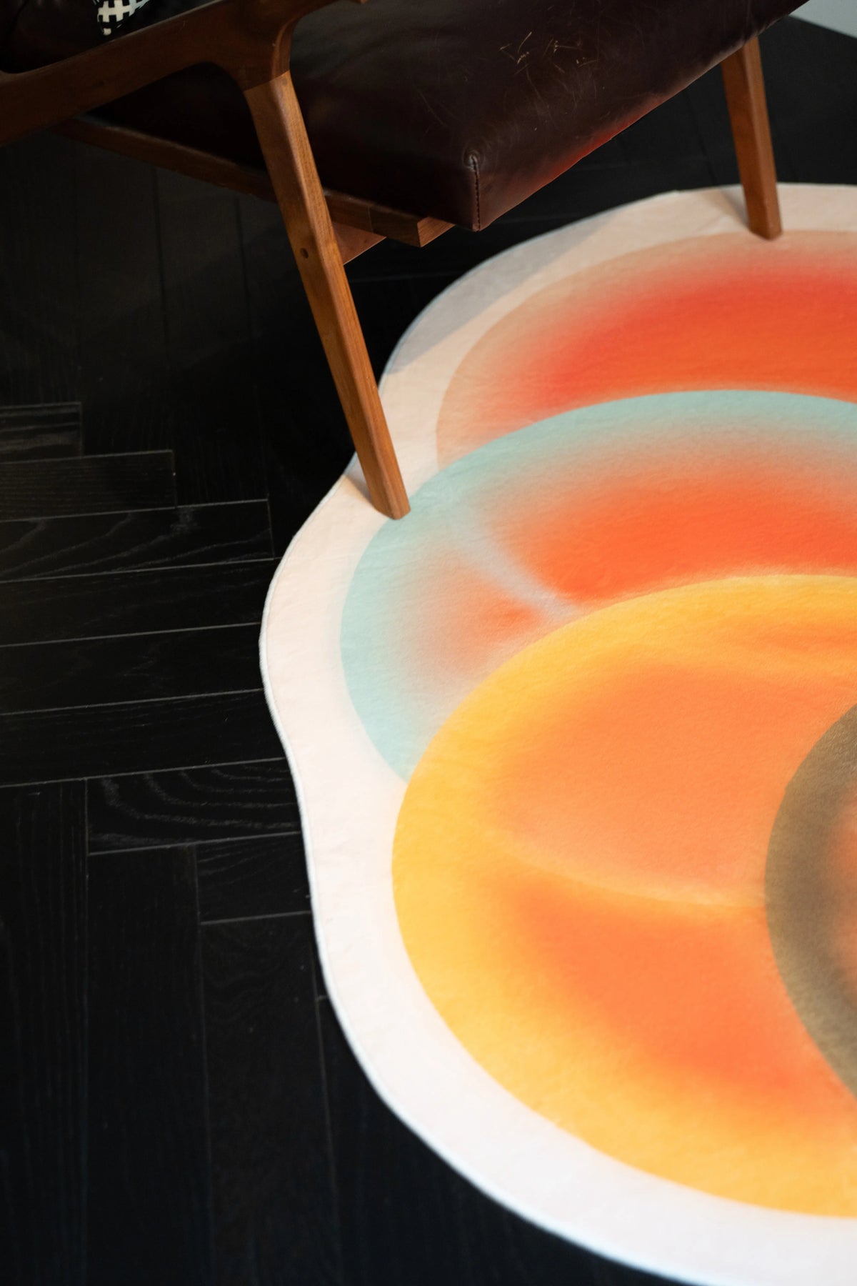 Abstract circle rug under a wooden chair leg showing overlapping orange and cream circles