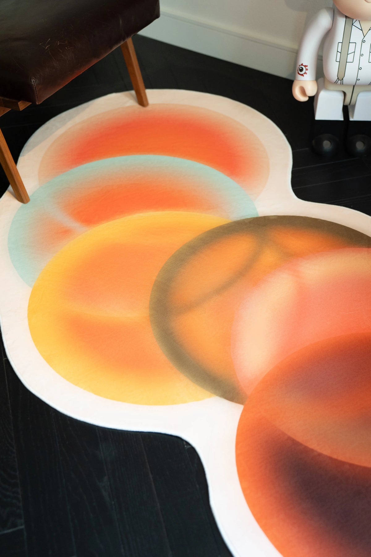 Earth tone abstract rug with layered circular forms in orange, yellow, and brown on a dark wood floor