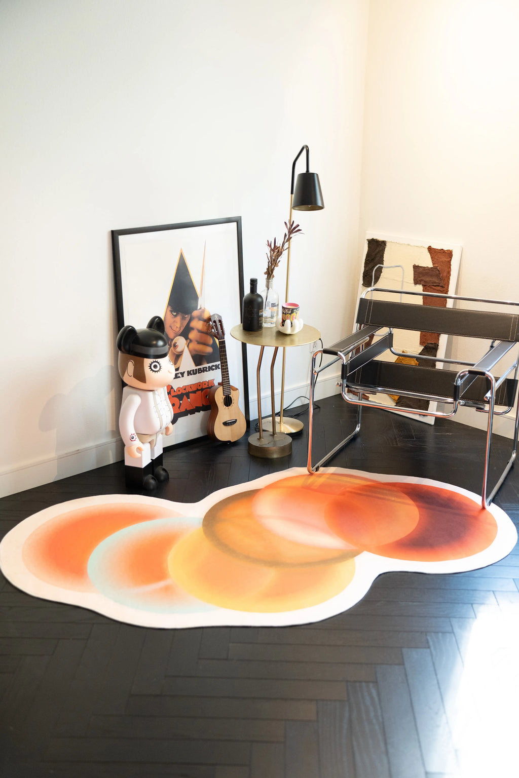Abstract circle rug in earth tones styled in a minimalist corner with a chrome chair, guitar, and framed artwork