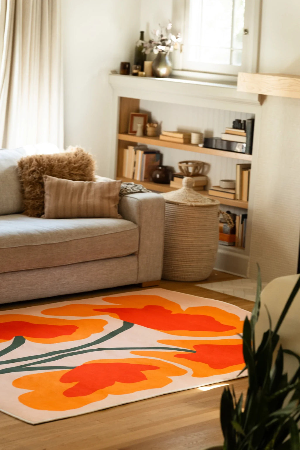 Partial view of the rug beside a beige sofa and open shelving, with oversized orange petals on a cream ground