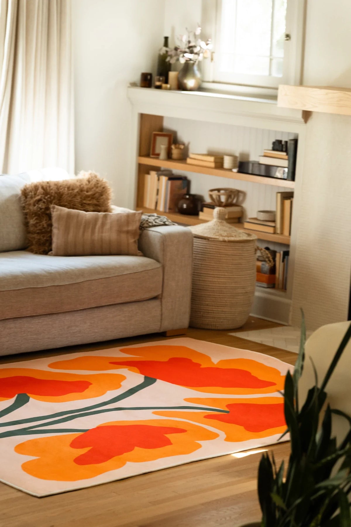 Partial view of the rug beside a beige sofa and open shelving, with oversized orange petals on a cream ground