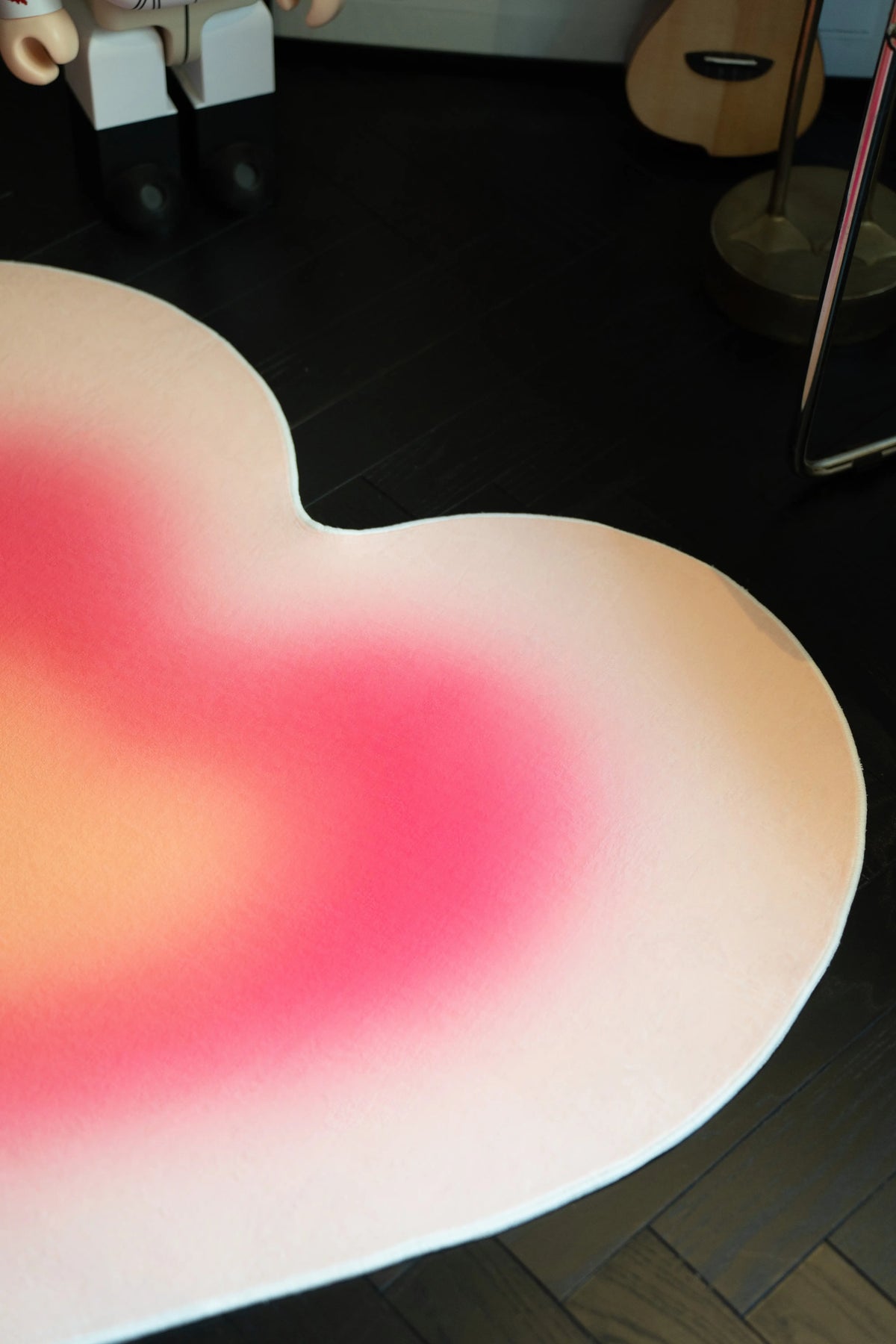 Partial close up of the pink heart rug with smooth color transitions beside a chair leg and guitar