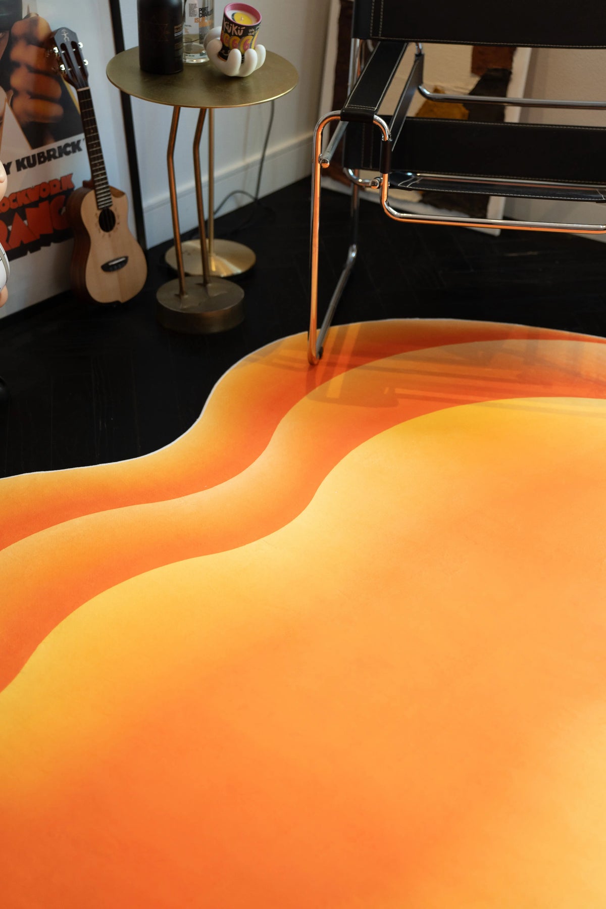 Orange abstract rug in a modern corner with a chrome chair, guitar, side table, and dark wood floor