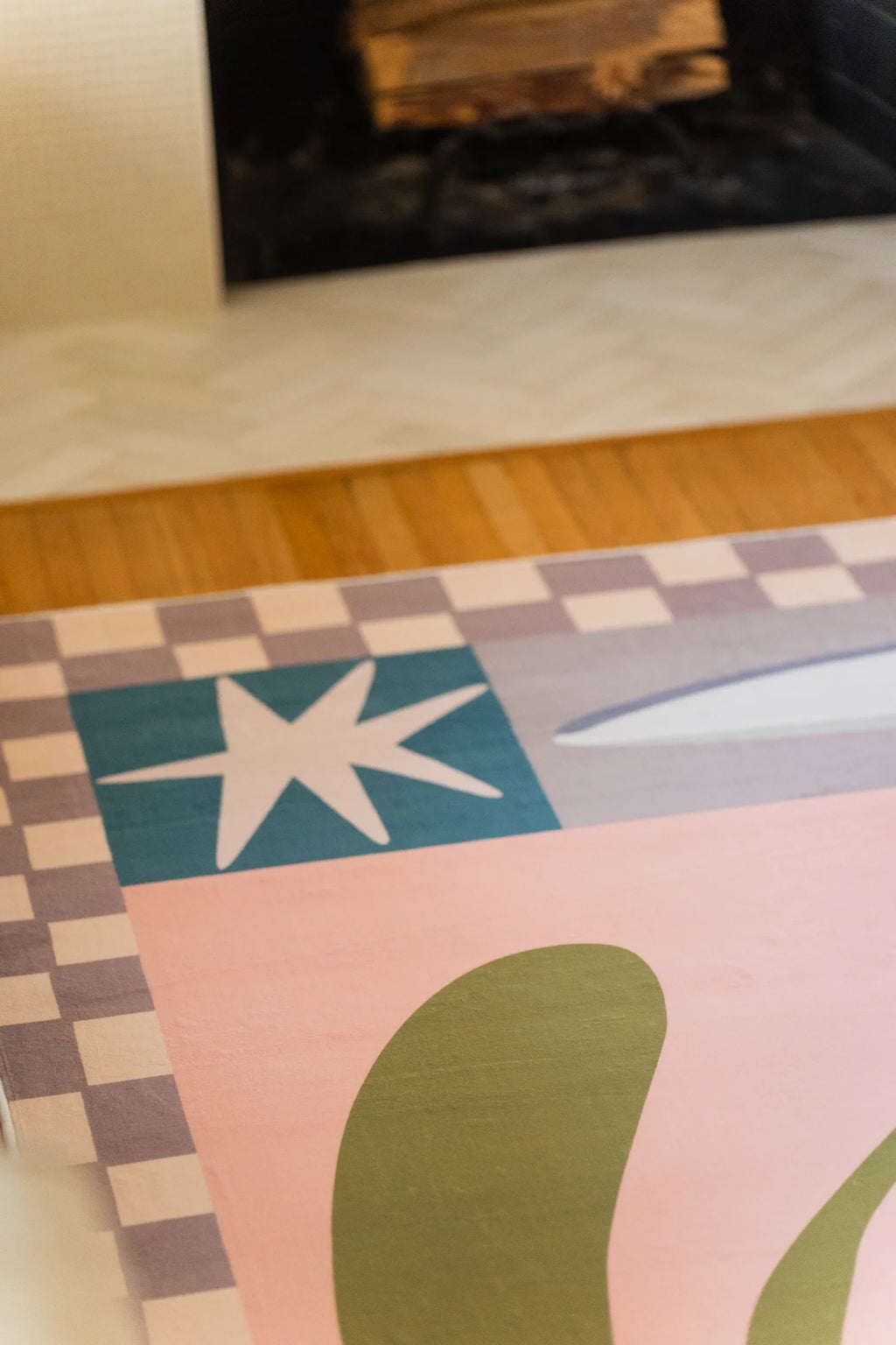 Corner detail of the floral checkered rug with a blue star block, olive leaf shape, and blush pink background