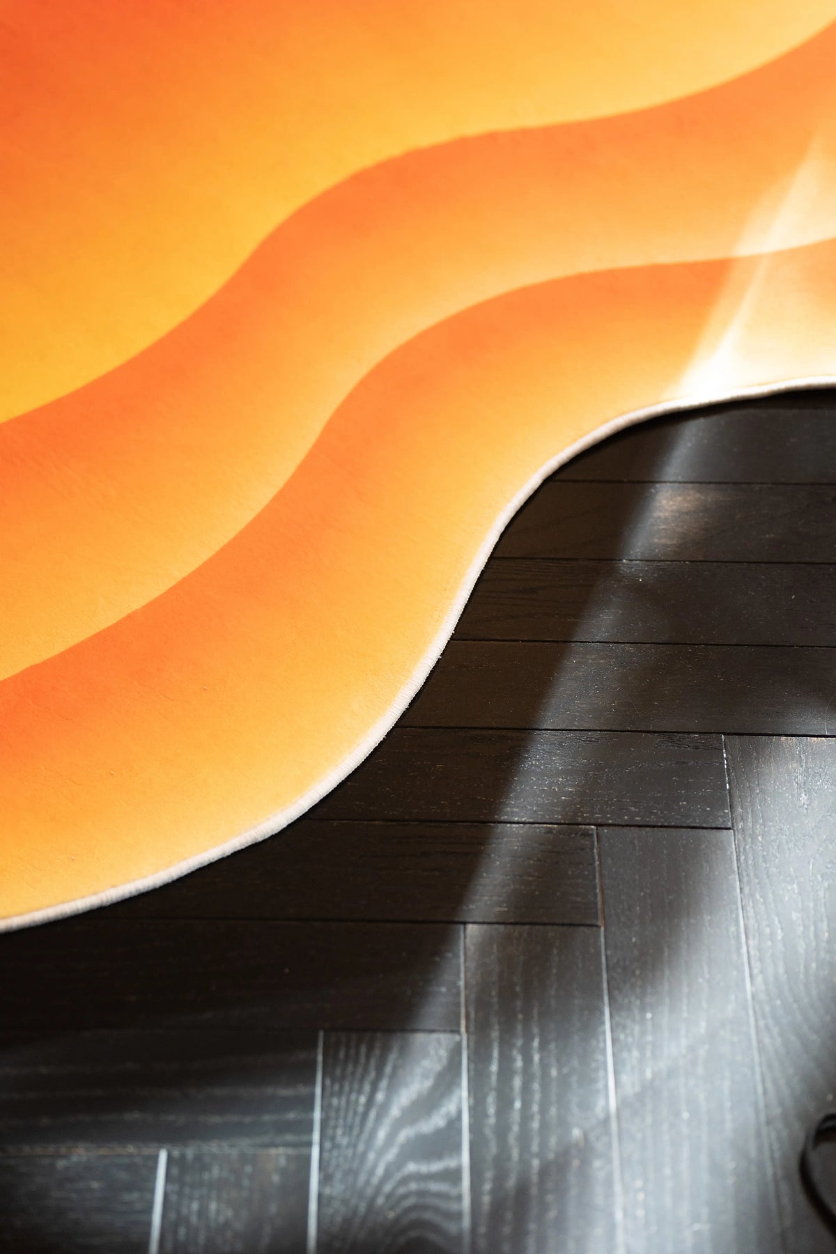 Close up of the rug edge showing flowing orange and yellow waves with sunlight across the dark floor