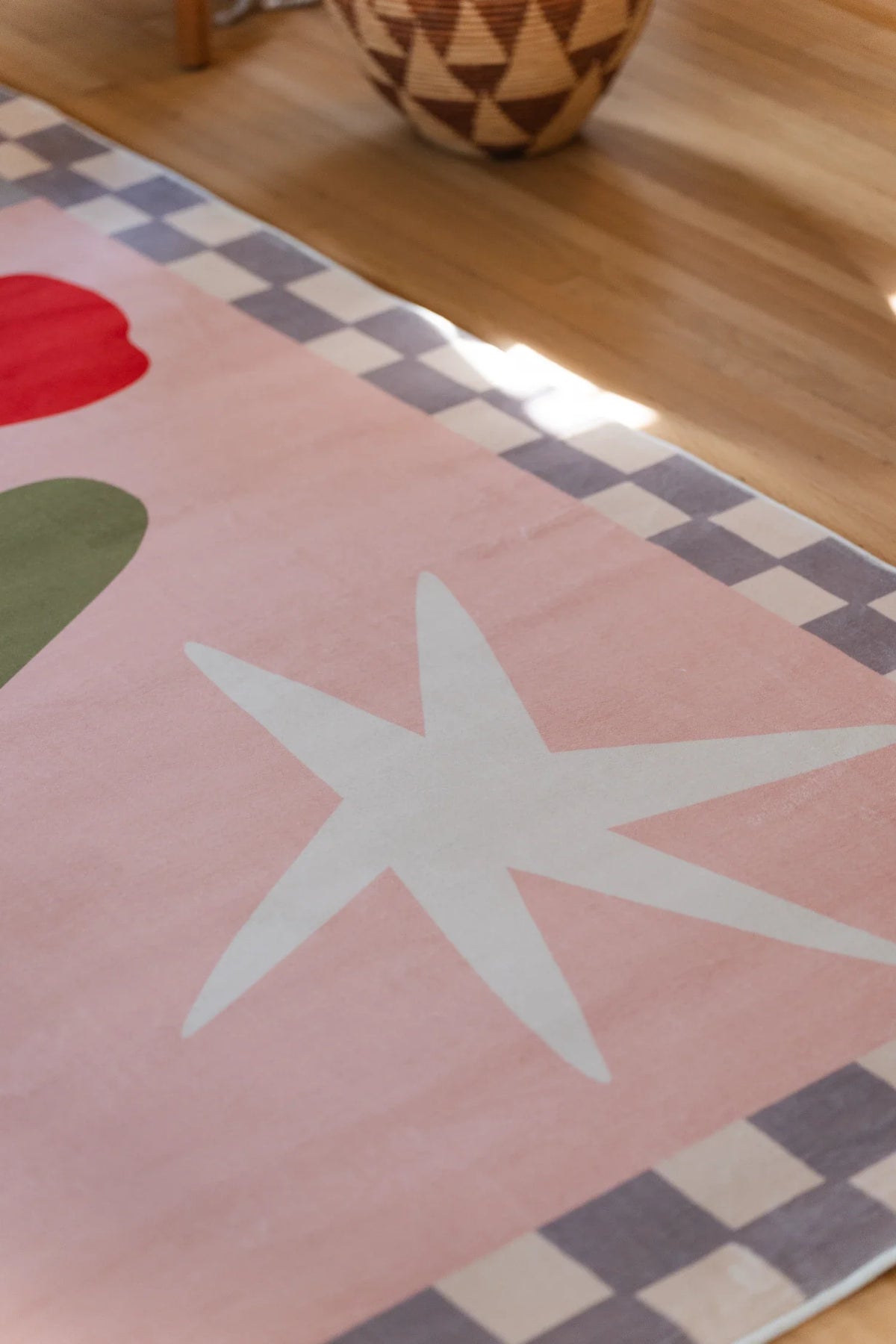 Close view of the vintage checkered floral rug with a white star motif and muted checker edge on a light wood floor