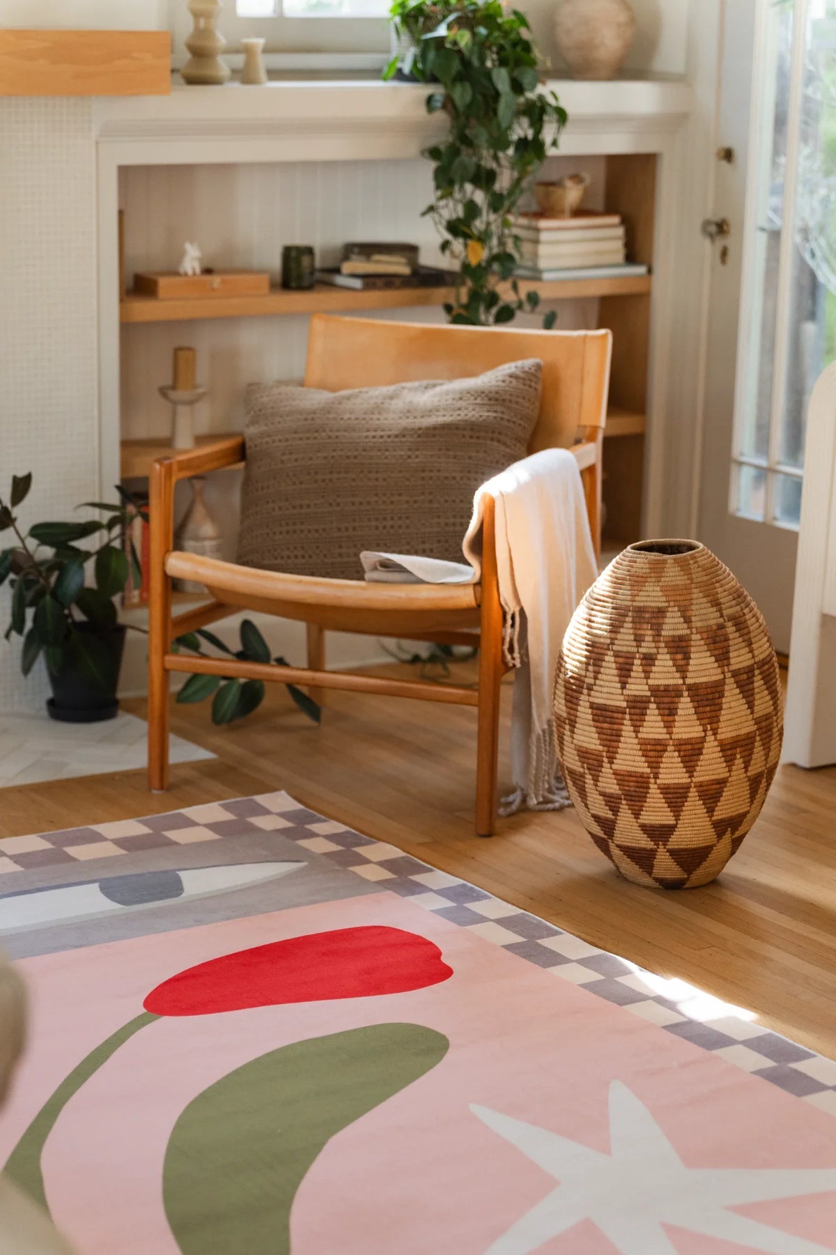 Vintage floral area rug beside a wood chair and woven basket, with a blush field, checkered border, and white star shape