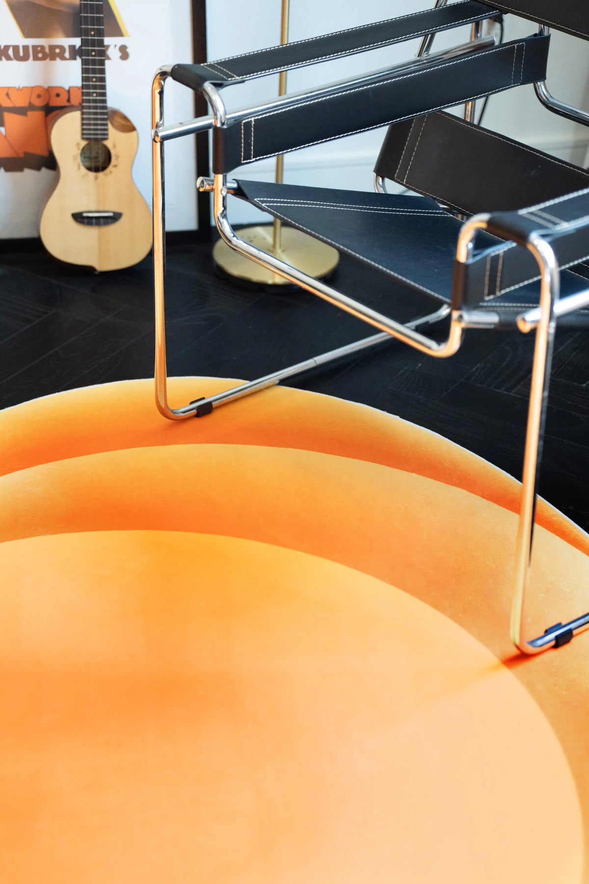 Partial view of the orange wavy rug beside a chrome chair and guitar in a modern reading corner