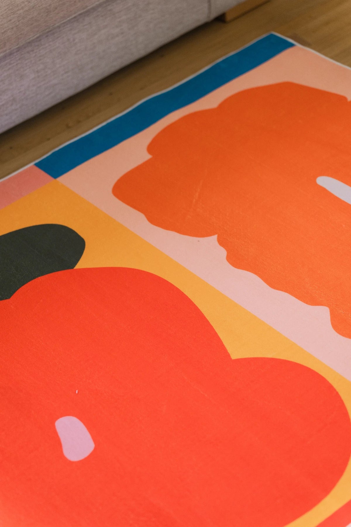 Corner detail of the abstract floral rug with a large orange petal block framed by a blue border on the wood floor