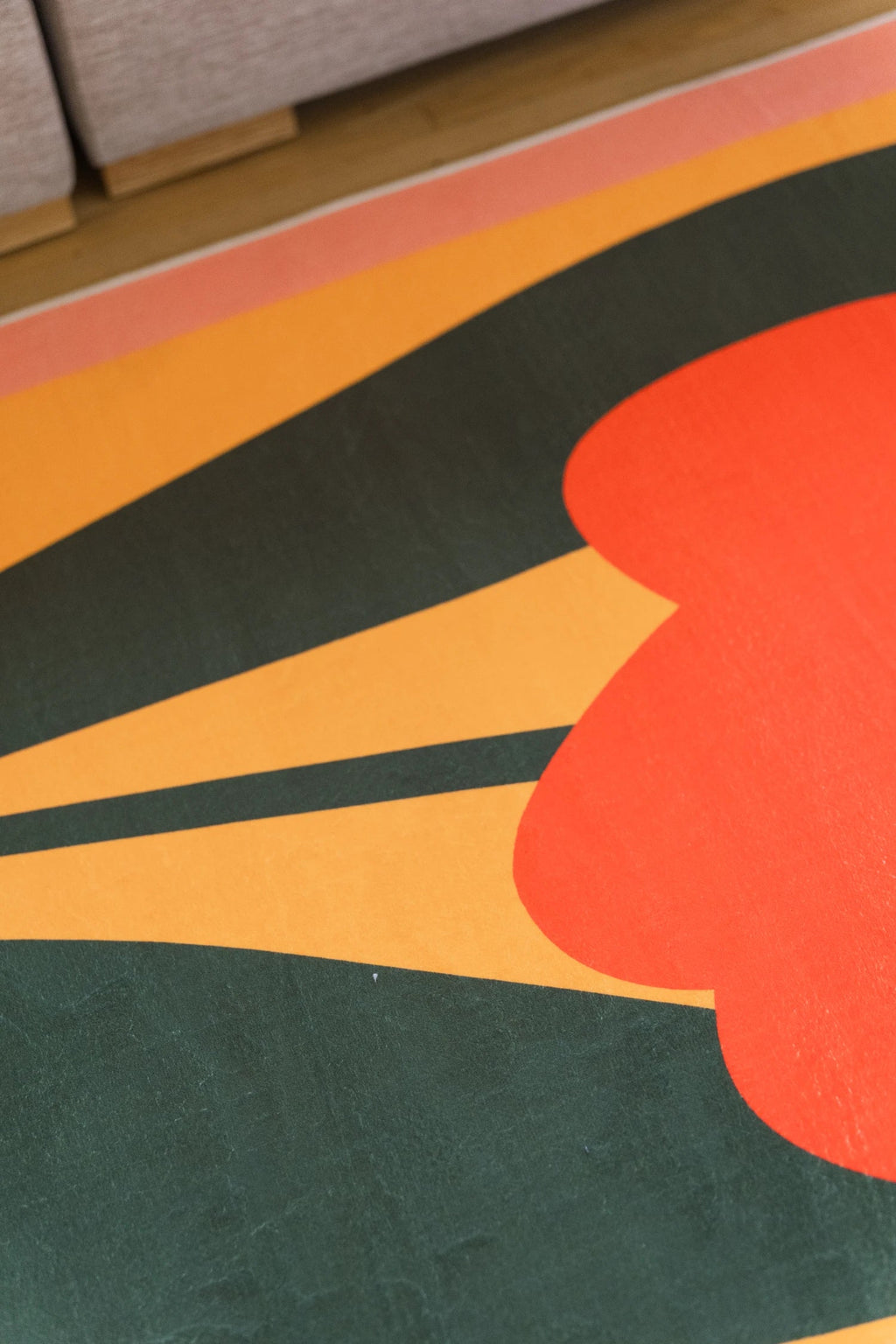 Close crop of the rug showing a dark green leaf form beside a rounded orange flower on a graphic color block field