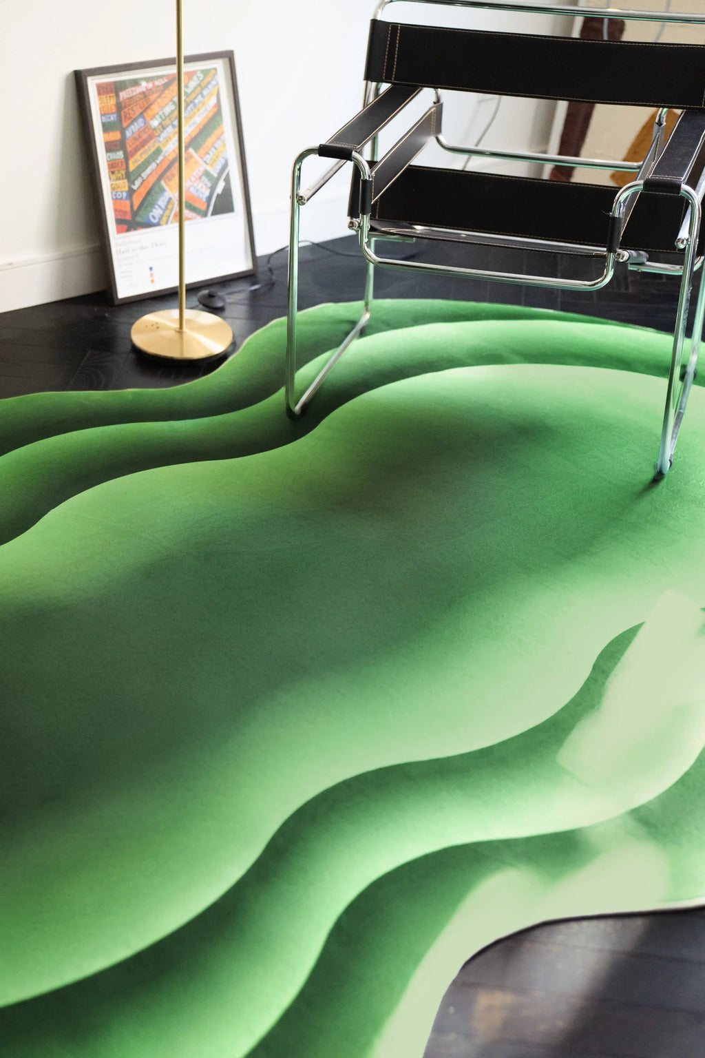 Close up of the green wavy rug beneath a chrome chair with a floor lamp and framed art in the background