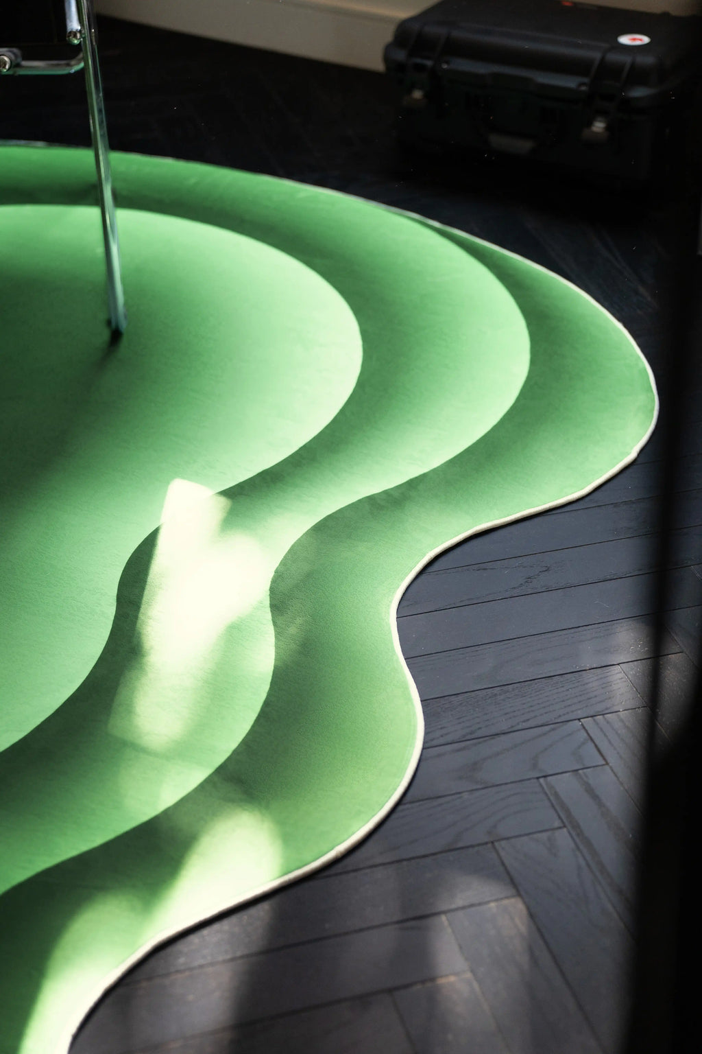 Partial view of the green abstract rug on a dark herringbone floor with sunlight across the curved edge