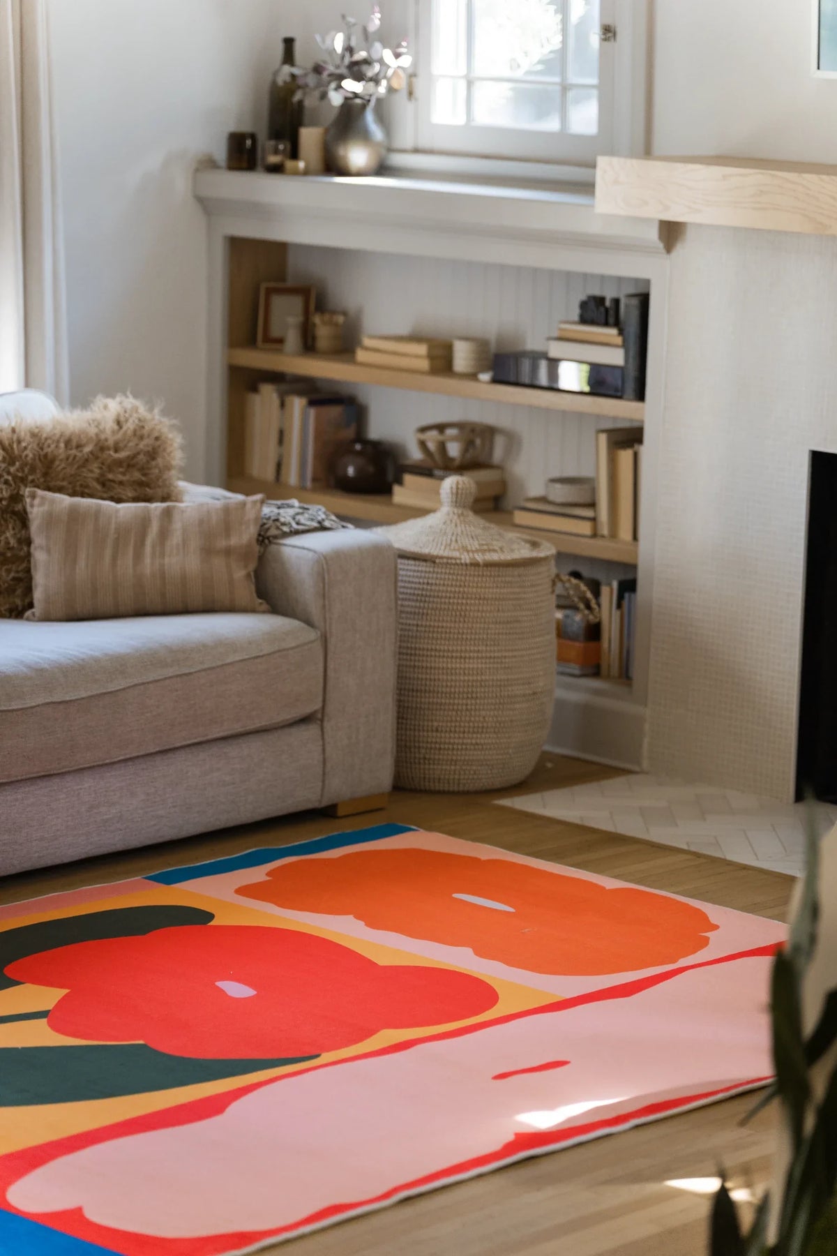 Partial crop beside a beige sofa and low shelf, with oversized orange red petals spreading across the rug on a light wood floor