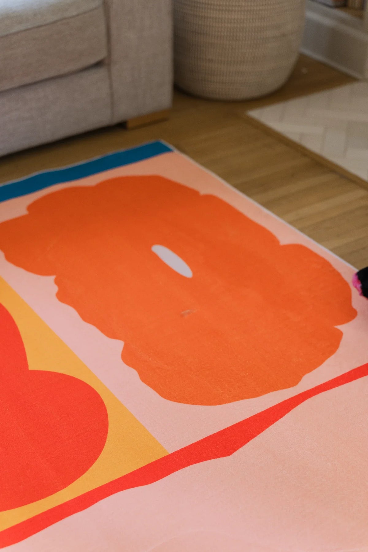 Modern floral area rug beneath a beige sofa, with a broad pink petal shape and thin red contour line