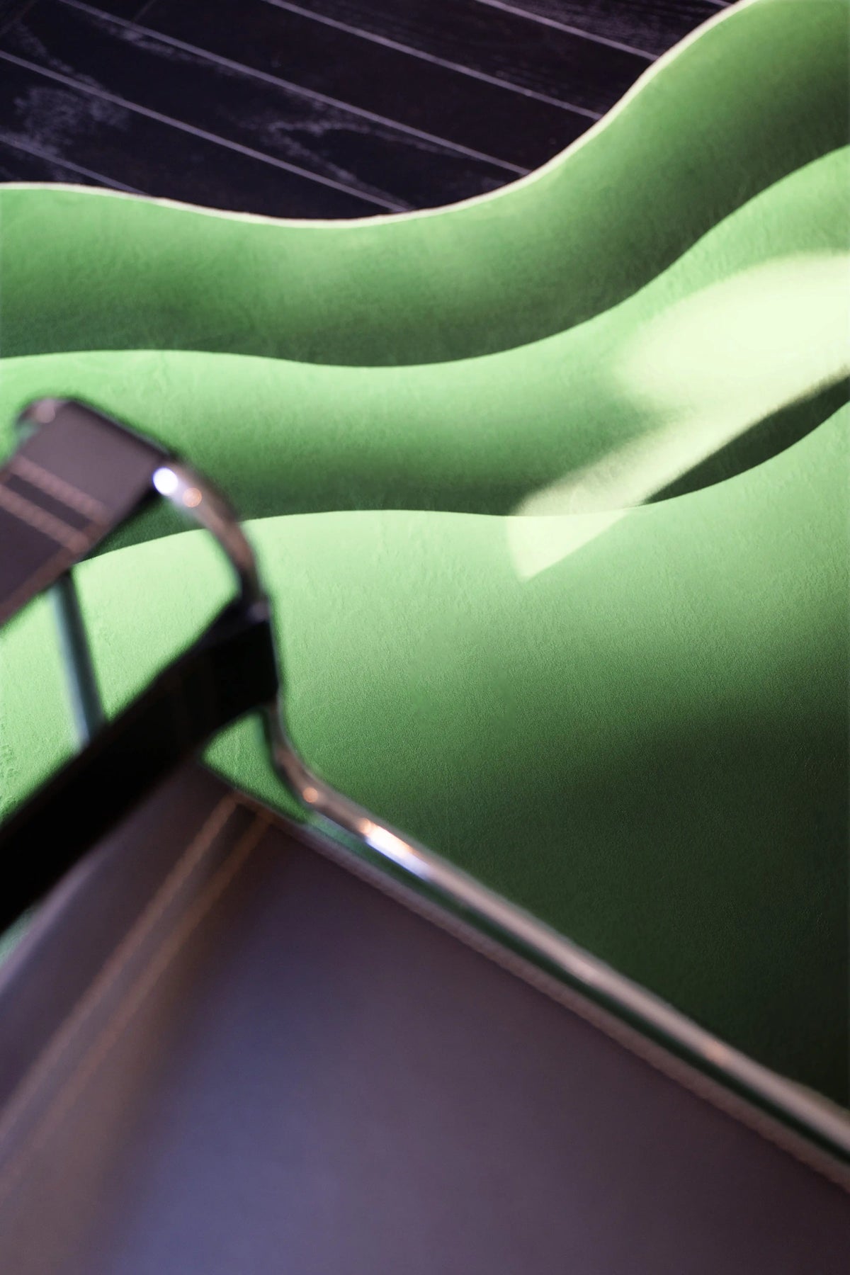Close up of the green wavy rug with layered curves and a chrome chair frame crossing the foreground