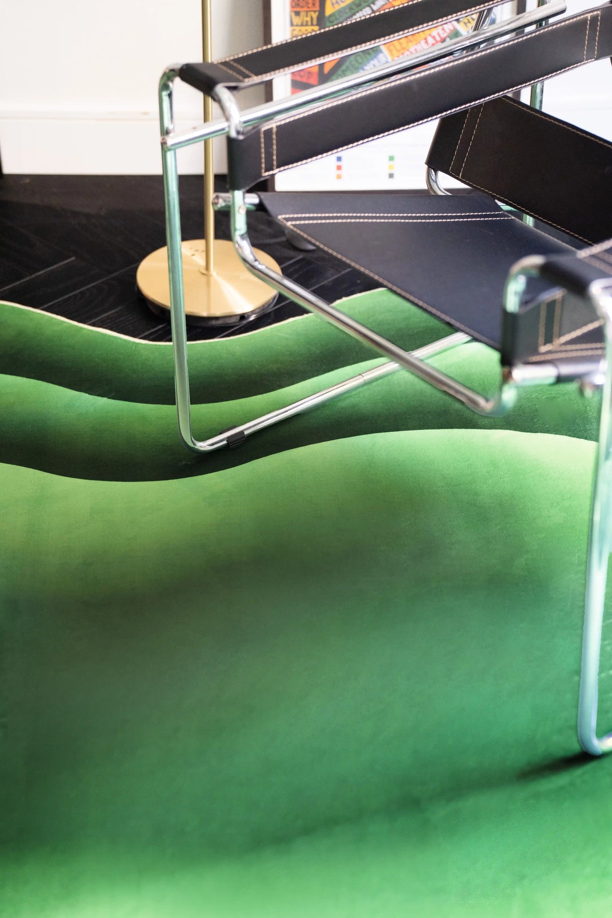 Green abstract rug beneath a chrome chair, showing soft tonal waves and rounded edges on a dark wood floor