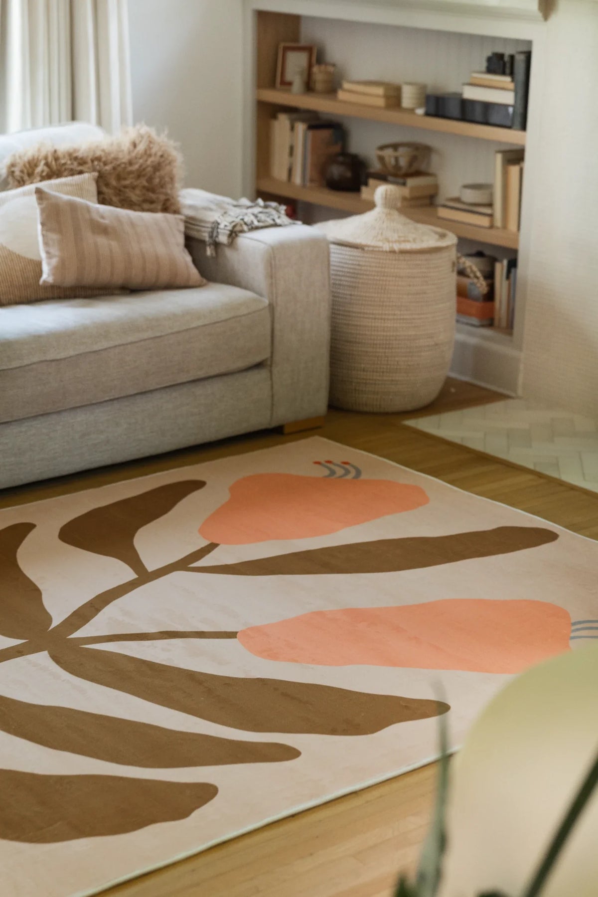 Partial view beneath a neutral sofa and open shelving, showing the vintage flower rug with peach petals and broad brown leaves