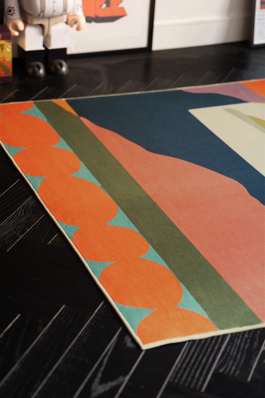Close up of the rug corner with an orange scalloped edge, coral field, and green stripe on dark wood floor