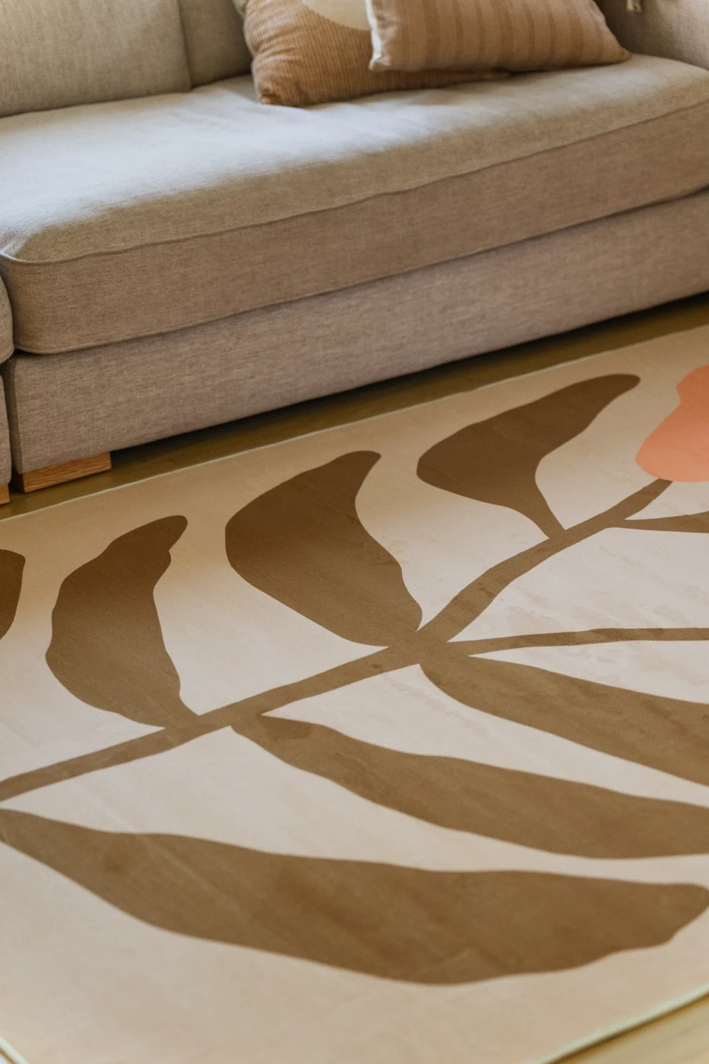 Partial crop of the rug beside a neutral sofa and woven basket, showing simplified flower forms in a relaxed modern interior