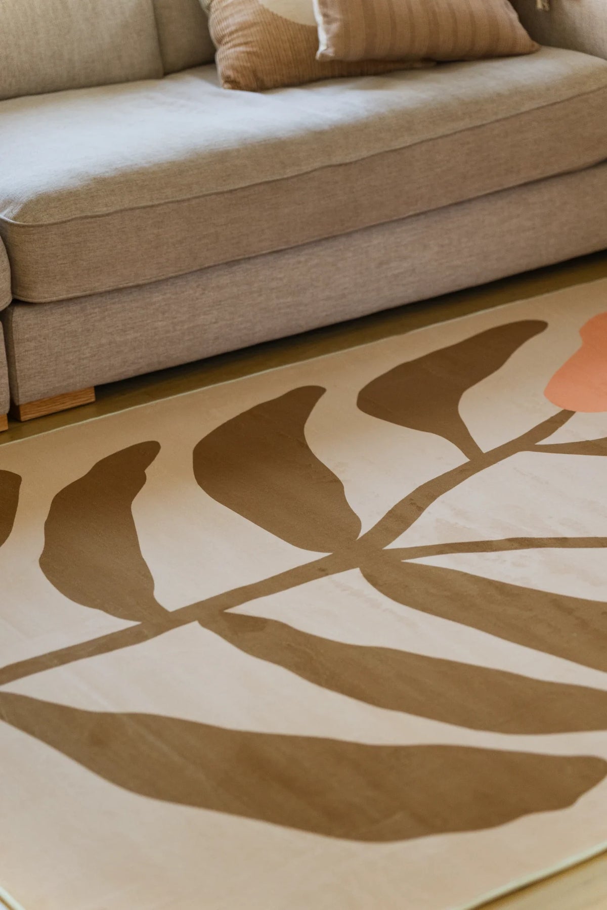 Partial crop of the rug beside a neutral sofa and woven basket, showing simplified flower forms in a relaxed modern interior