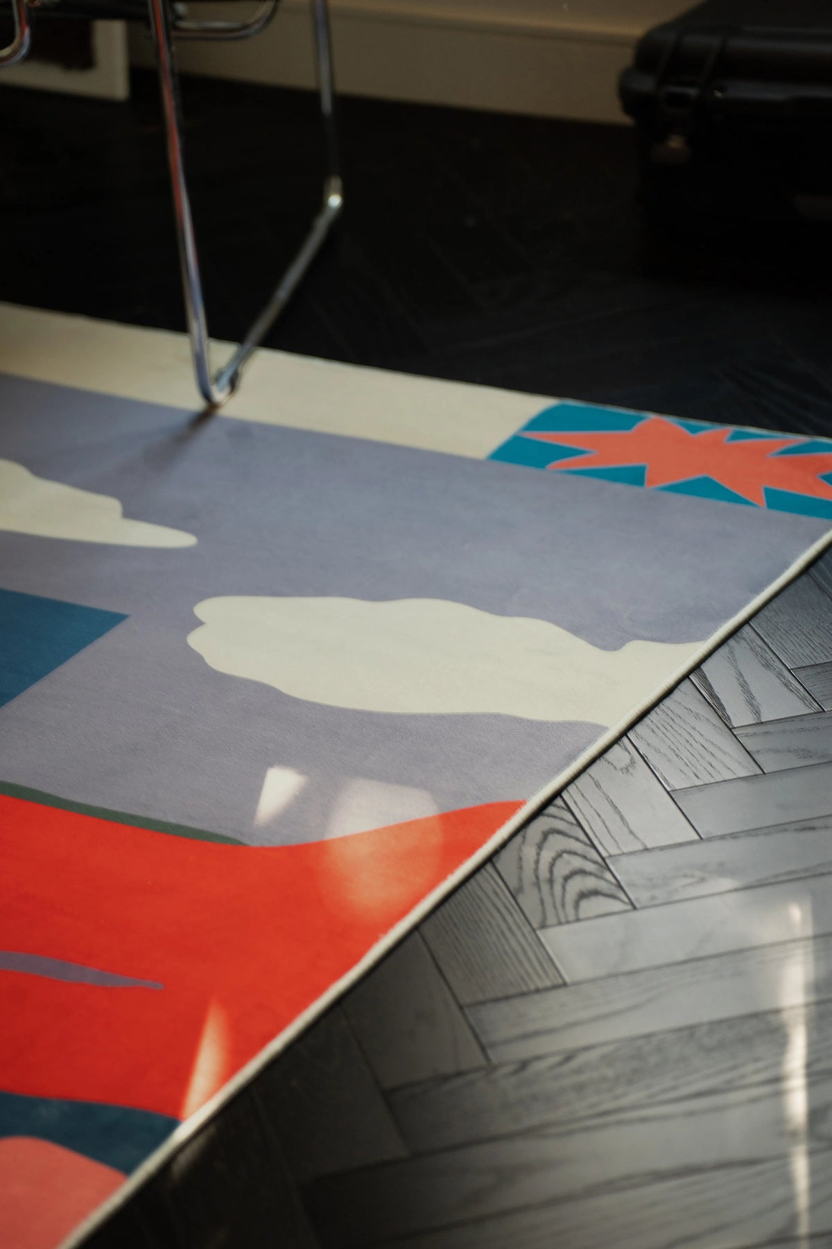 Vintage Landscape rug beside a chrome chair, showing the blue field and orange scalloped border on a dark floor