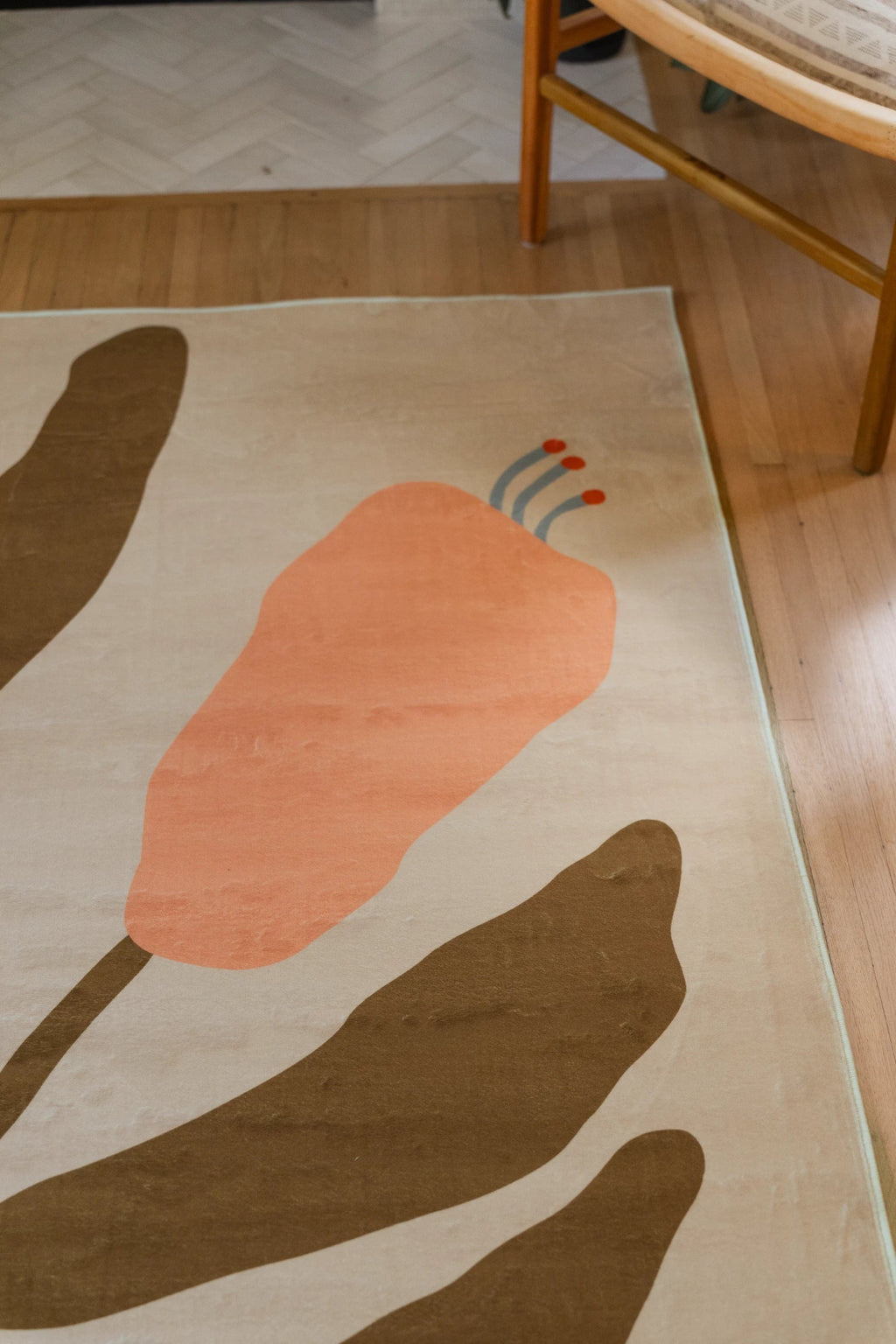 Top corner of the Beige Vintage Flower Rug near a wood chair, showing a peach flower bud and layered brown leaves