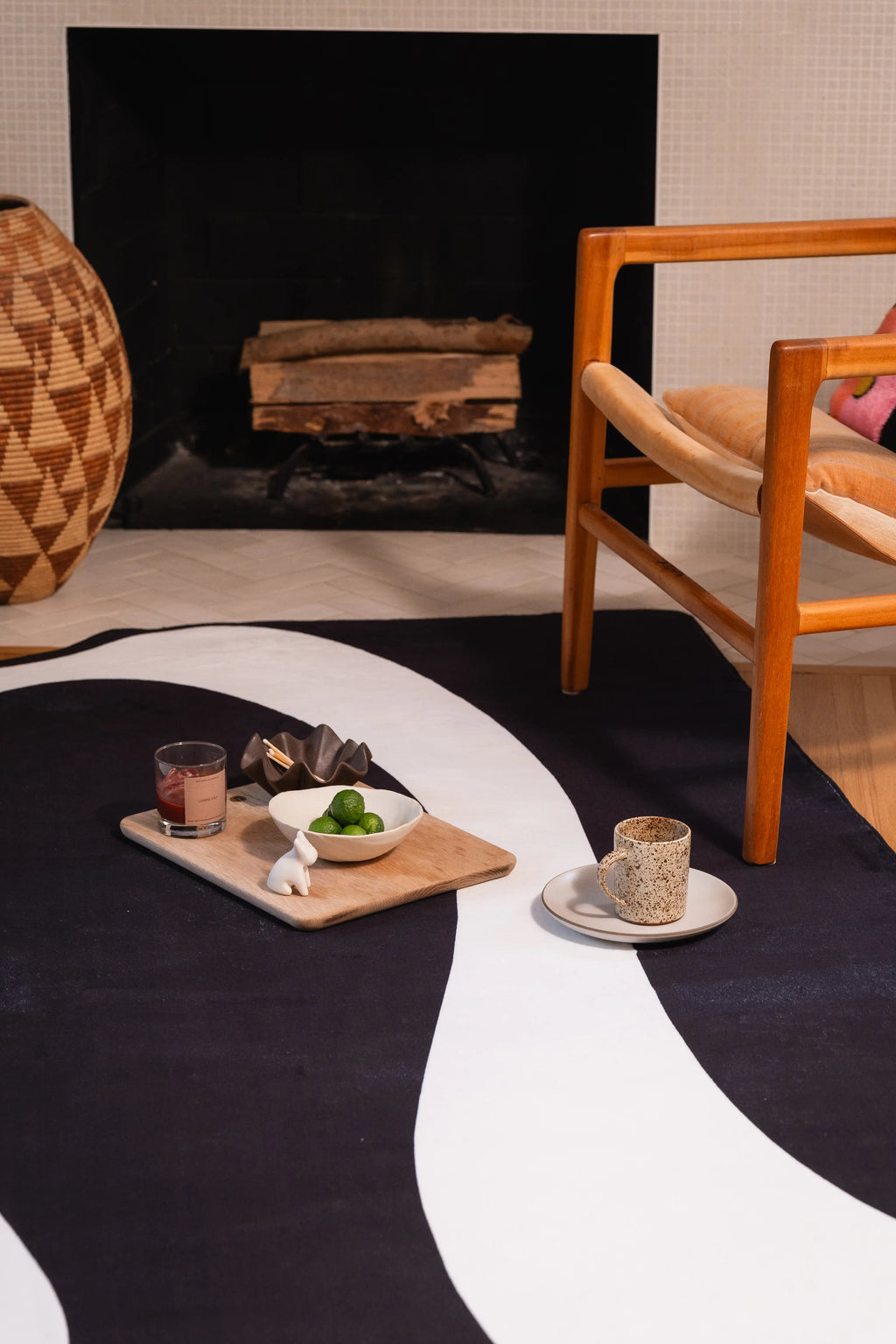 Black and white melting-pattern rug in front of a fireplace with two serving trays and a wooden chair.