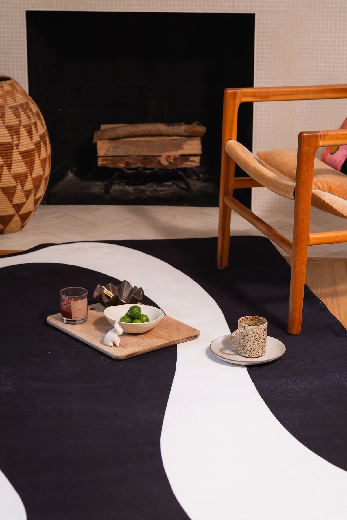 Black and white melting-pattern rug in front of a fireplace with two serving trays and a wooden chair.