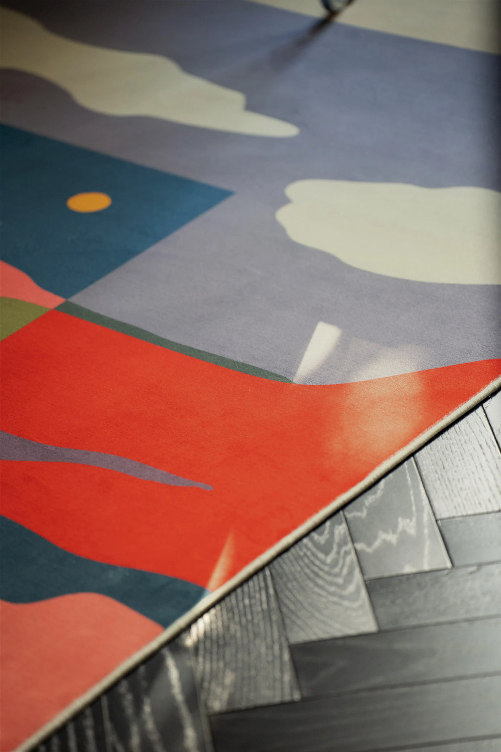 Corner view of the landscape area rug on a dark wood floor with blue, cream, and coral painted shapes