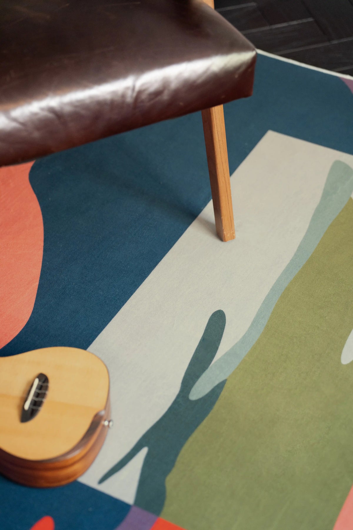 Vintage Landscape Area Rug under a brown leather bench with a guitar nearby, showing the layered painted motif