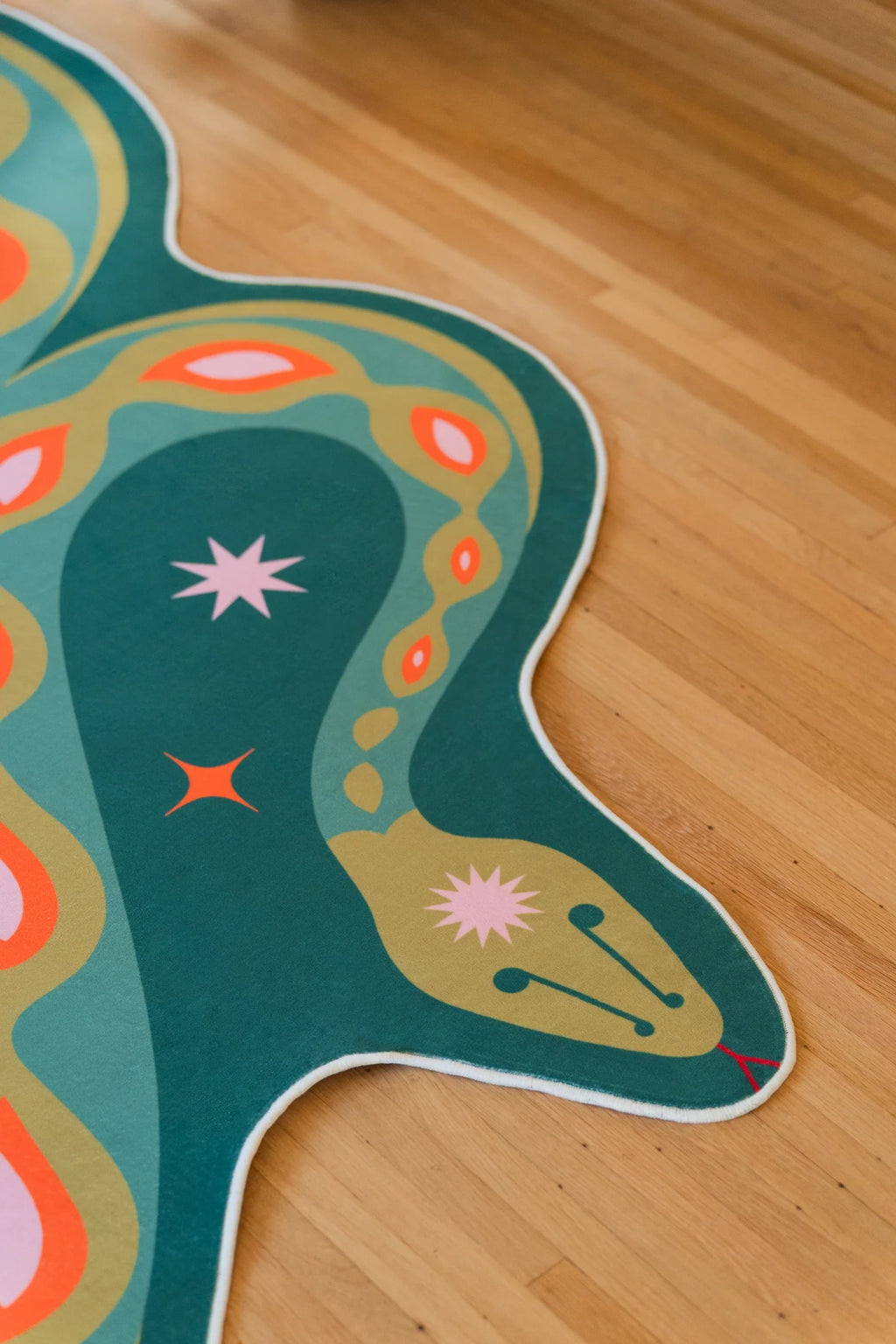 Close up of the deep green snake rug on a light wood floor, showing star motifs and rounded orange markings